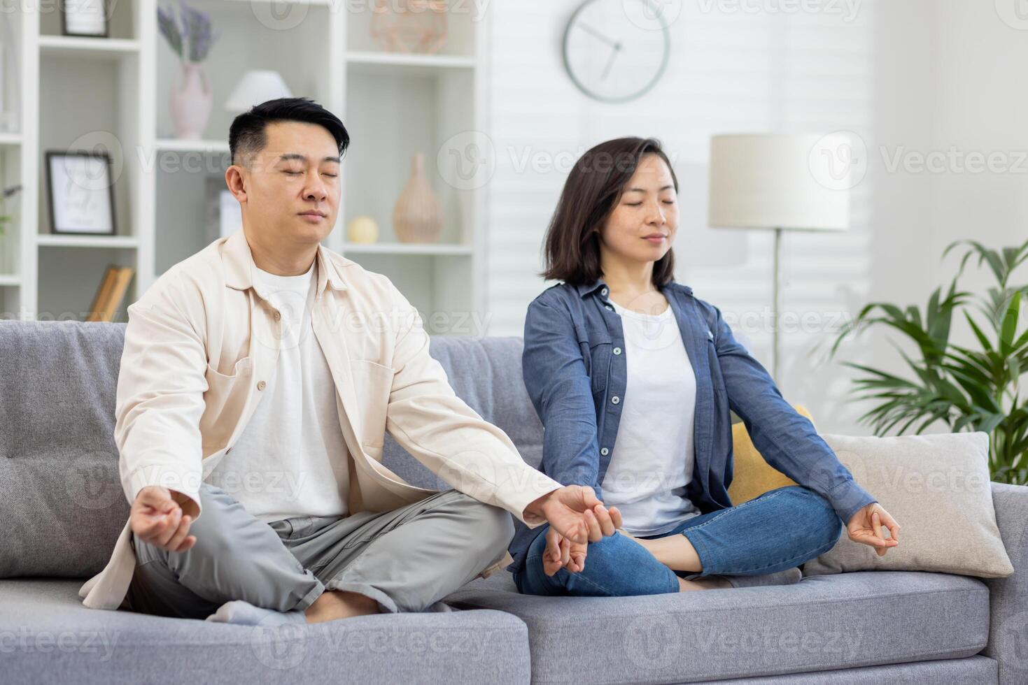 Happy asian family at home on sofa meditating, couple man and woman sitting in lotus position in living room with closed eyes resting relaxing together. photo