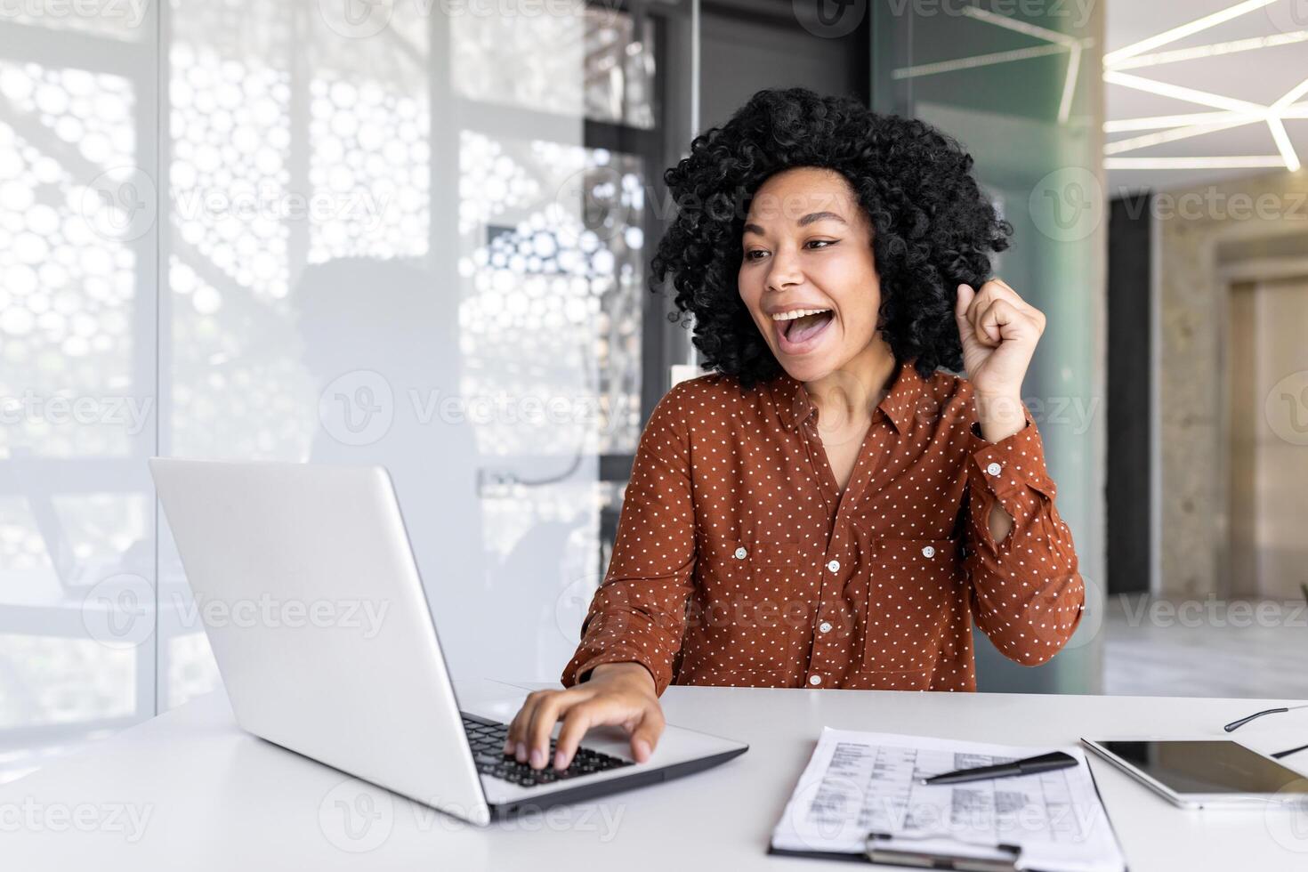 alegre exitoso satisfecho africano americano mujer de negocios celebrando genial logro resultados a lugar de trabajo dentro oficina, hembra trabajador celebrando participación mano arriba sonriente con ordenador portátil. foto
