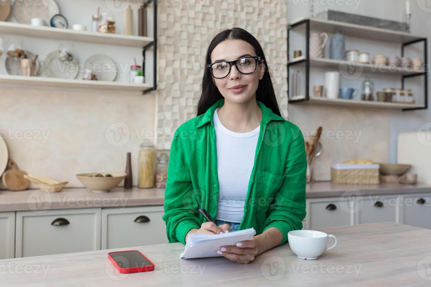 un mujer profesor en lentes sentado a hogar en frente de el cámara con cuaderno foto