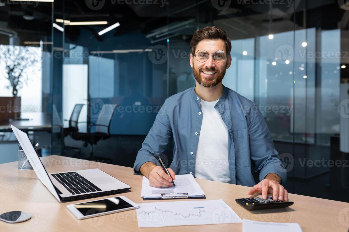Portrait of successful businessman behind paper work, man in shirt smiling and looking at camera, financier boss inside office using laptop in work at workplace. photo