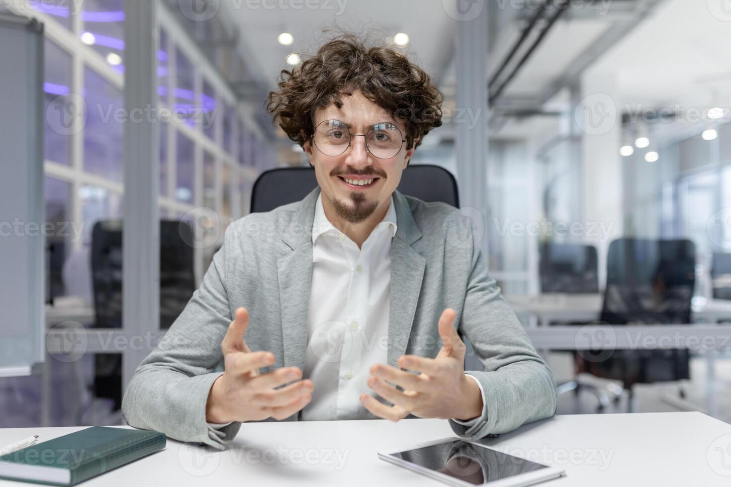 Engaged young professional with curly hair discussing ideas at his office workspace, embodying corporate enthusiasm and expertise. photo