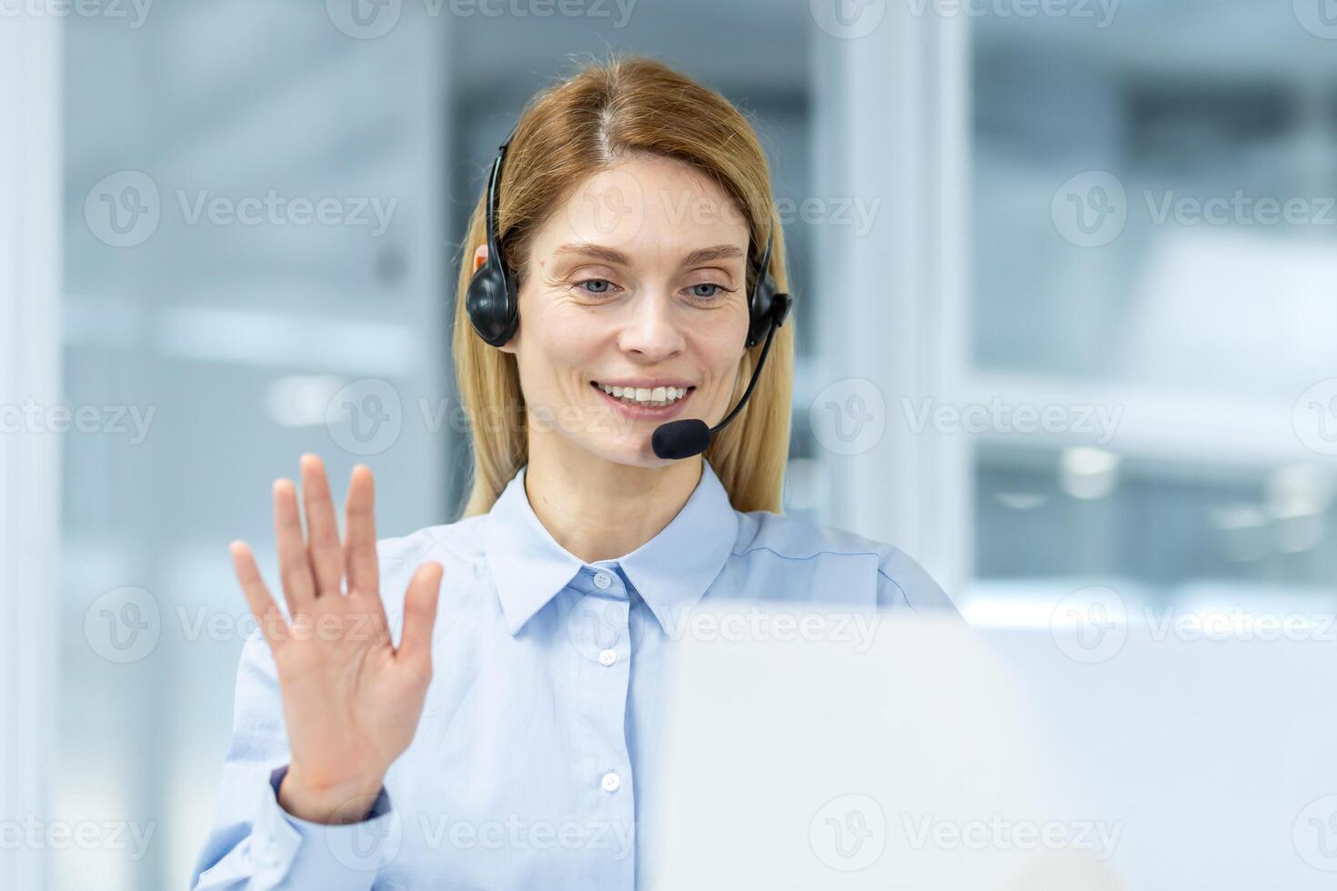 Friendly businesswoman with a headset making a cheerful greeting gesture during a conference in an office. photo