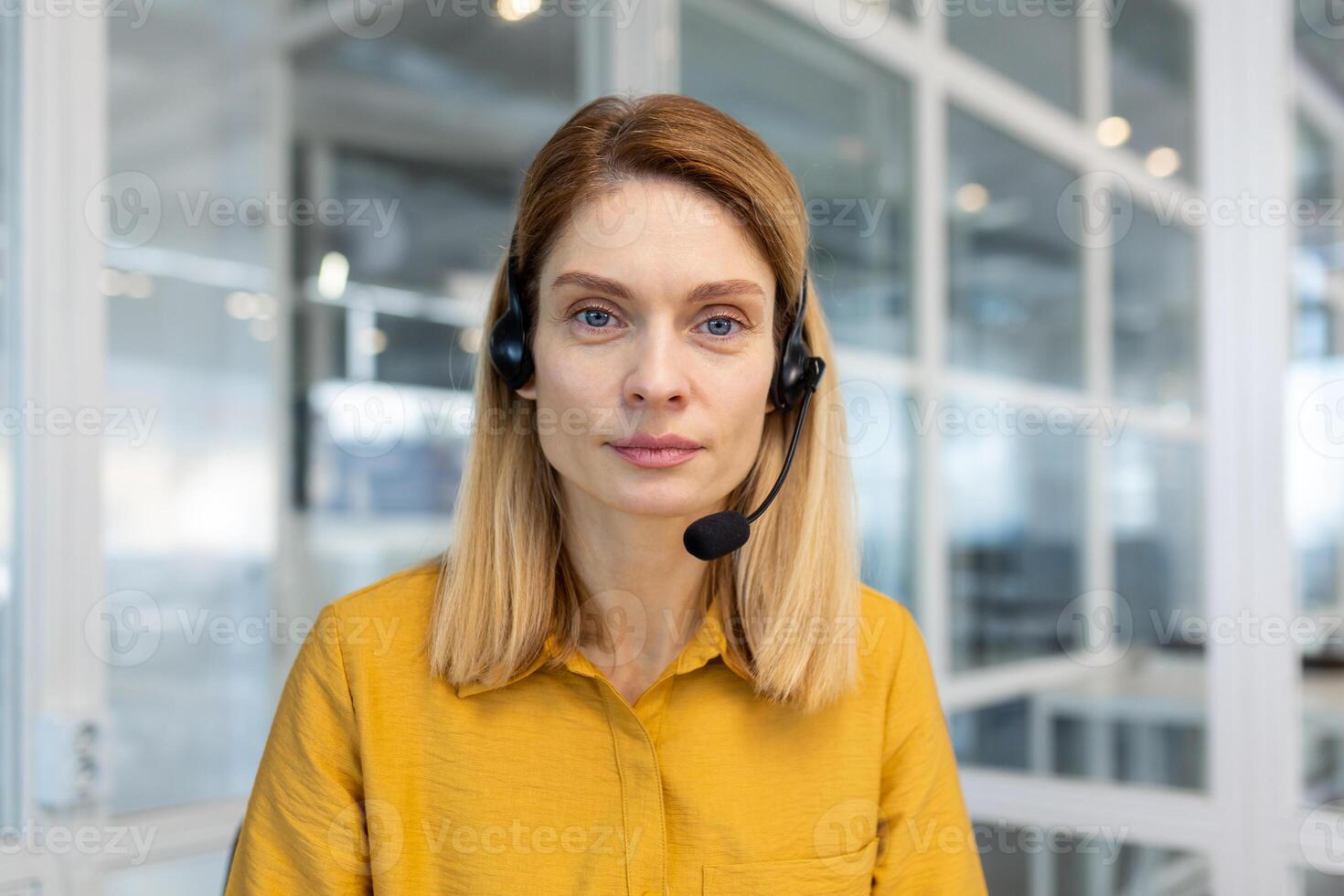 Web view camera, pov. Woman with a headset phone listens to the interlocutor, call, online meeting. The support service worker looks seriously and thoughtfully at camera, works inside office. photo