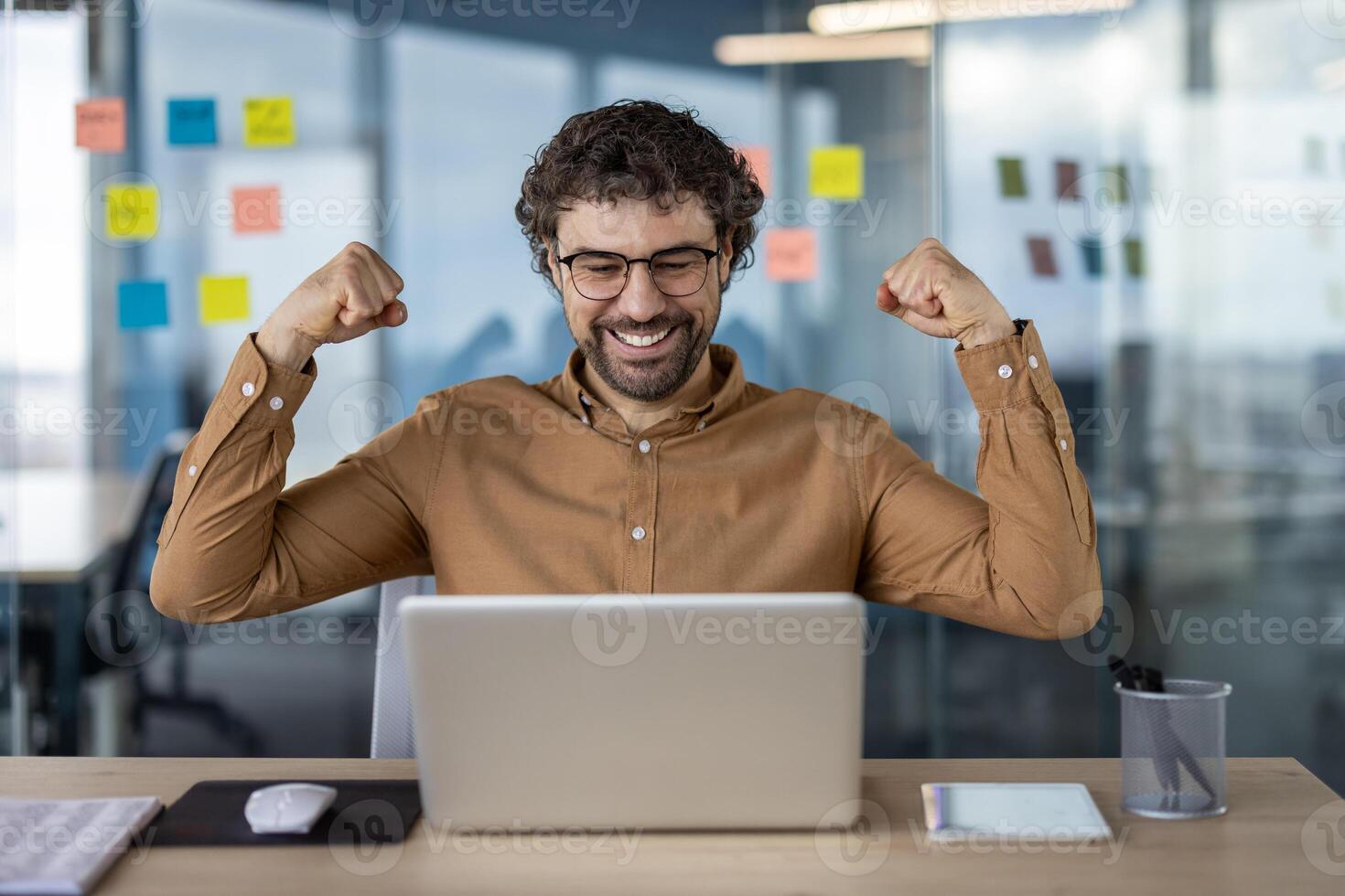 jubiloso masculino profesional en lentes celebrando un exitoso acuerdo o logro mientras trabajando en su ordenador portátil en un moderno oficina ajuste. foto