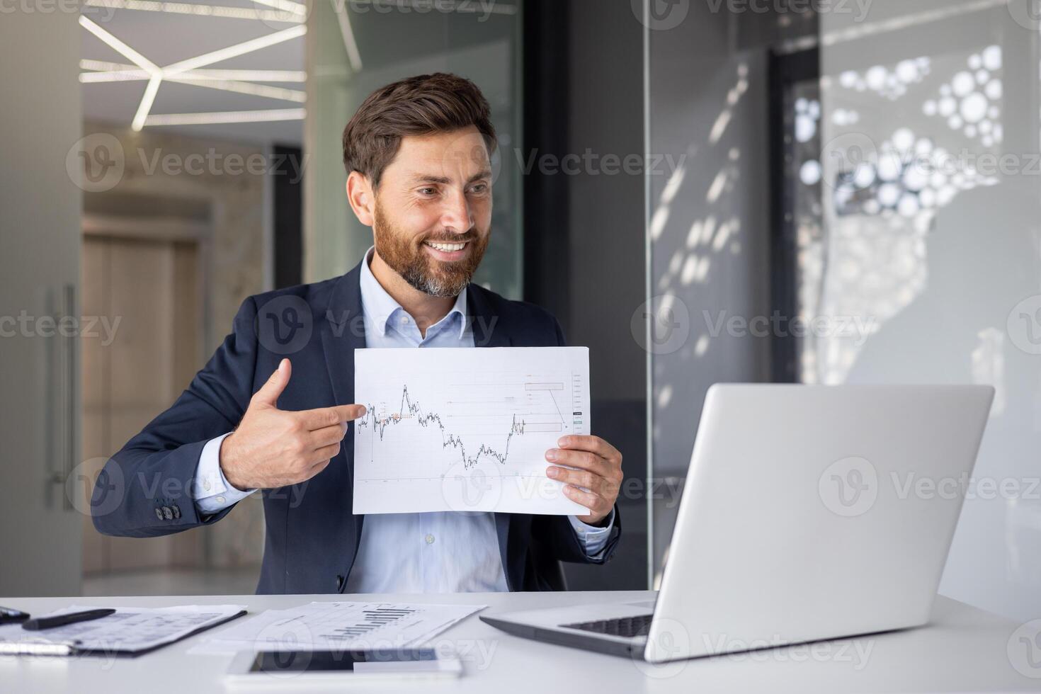 A cheerful businessman in a modern office presenting a graph during a virtual conference, exemplifying professionalism and engagement. photo