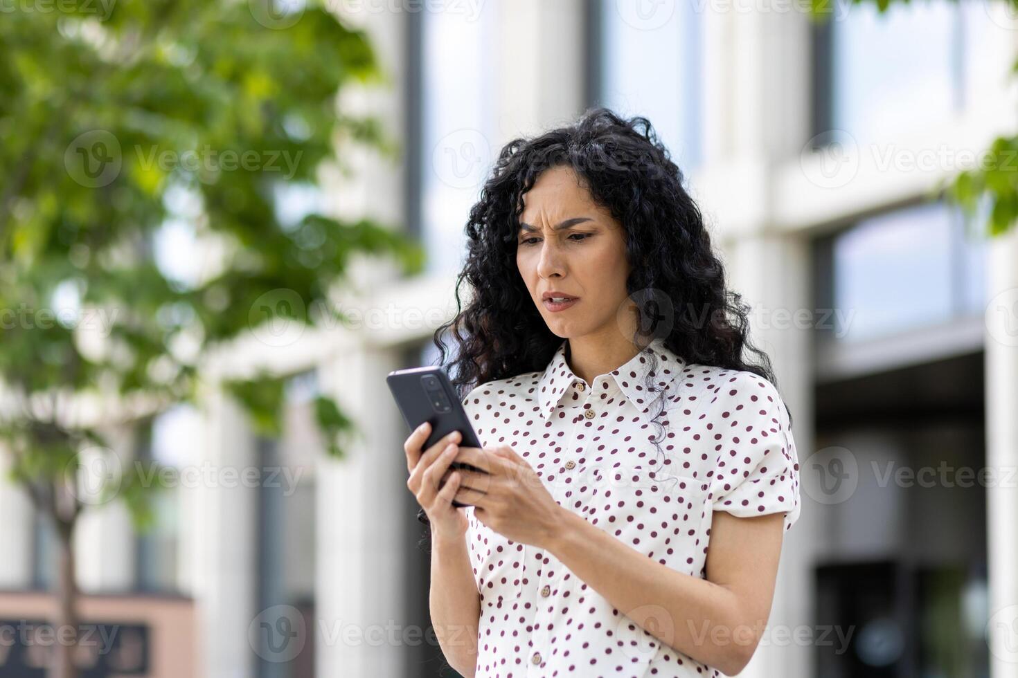 Sad disappointed woman received online notification with bad news on her phone, businesswoman walking outside office building, using application on smartphone, reading social media unsatisfied. photo