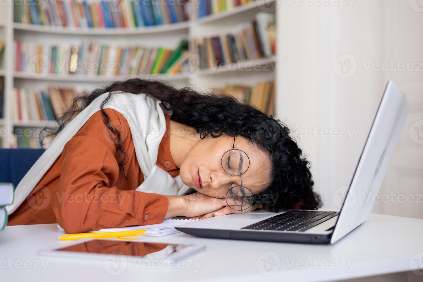 Young attractive female office worker wearing glasses fell asleep at workplace in front of laptop sitting at desk in office, overtired at work, overwork due to busy schedule. photo