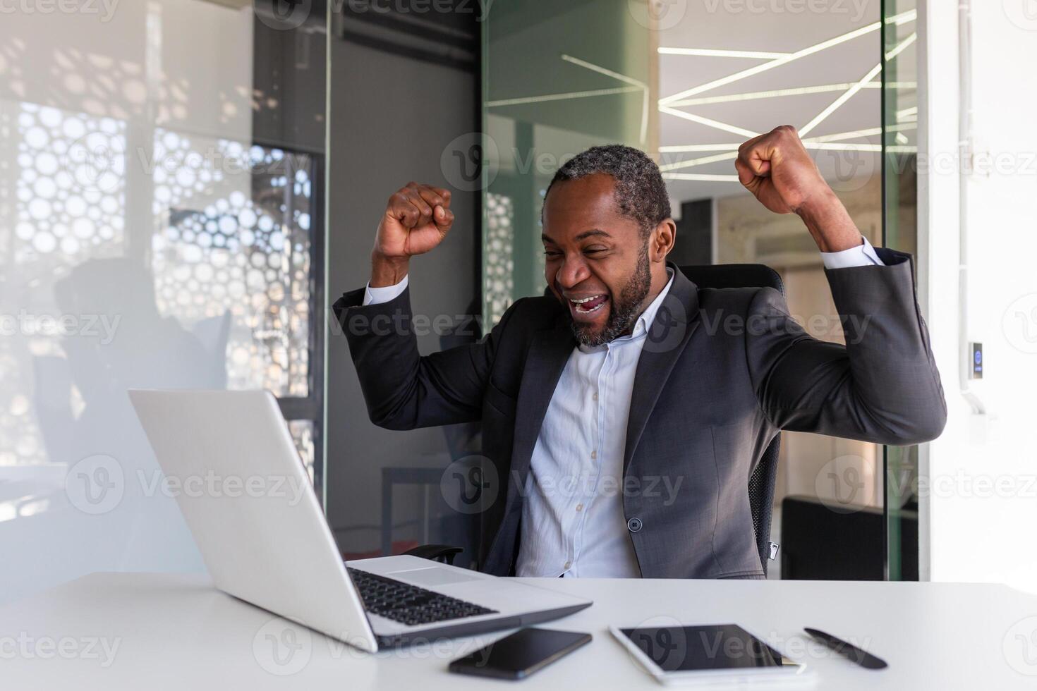 maduro experimentado empresario celebrando victoria éxito a lugar de trabajo, jefe dentro oficina contento con financiero resultados logro recibido en línea notificación ganar mensaje, participación manos arriba. foto