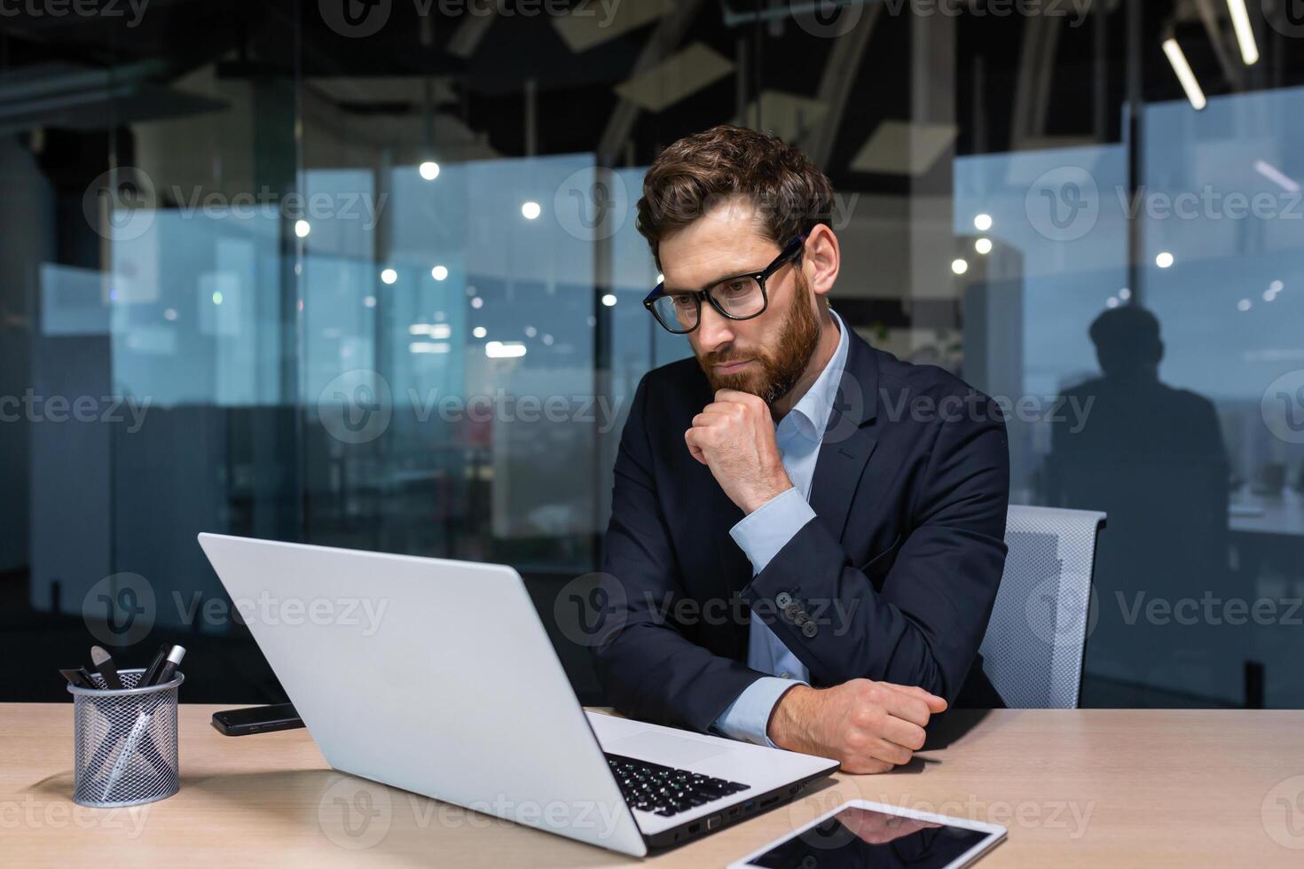 grave pensando empresario trabajando dentro oficina edificio, hombre reflexionando importante decisión, jefe en negocio traje utilizando ordenador portátil a trabajar. foto