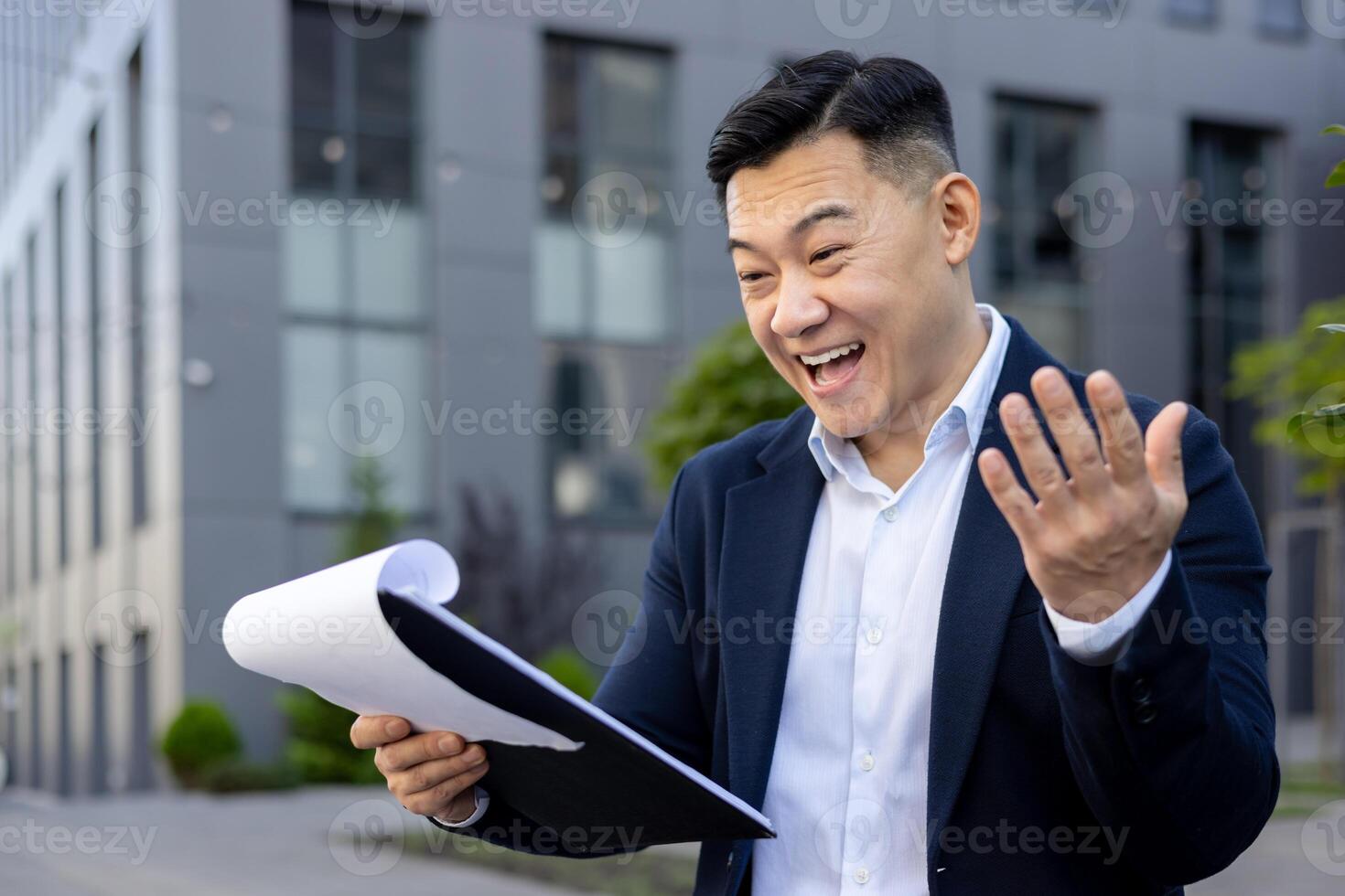 Professional man in a suit outside office buildings gesturing to stop while holding paperwork. photo