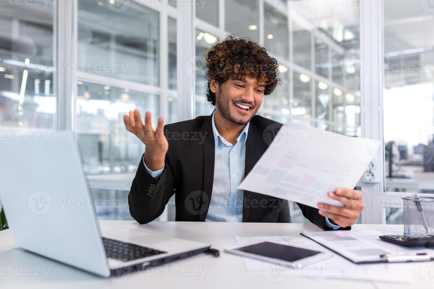Young successful financier investor inside office at workplace with documents and laptop, hispanic man in business suit looking at reports and graphs, businessman satisfied with achievement results. photo