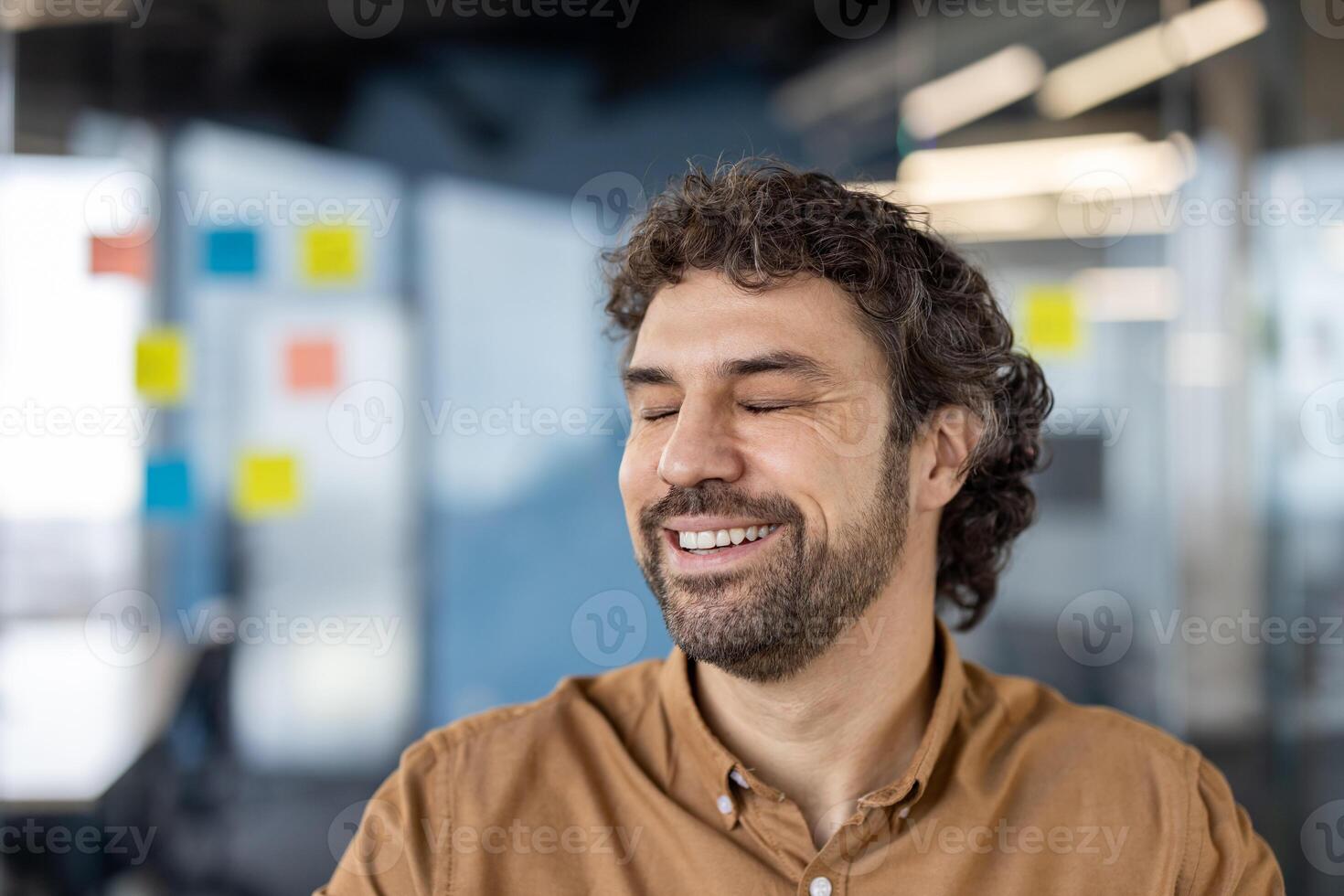 un alegre de edad mediana hombre con Rizado pelo sonriente ligeramente en un casual trabajo ambiente. él aparece contenido y a facilidad, sugerencia un cómodo y positivo oficina atmósfera. foto