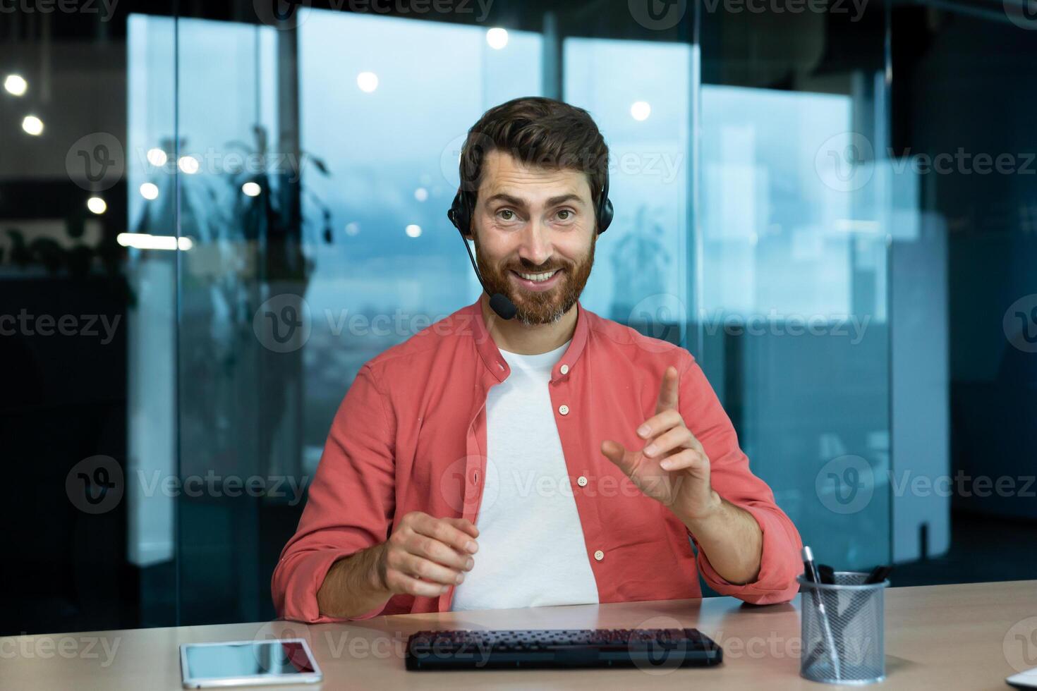 call, joyful smiling man with headset phone working in evening time inside office, web camera view, online meeting with colleagues partners remotely. photo