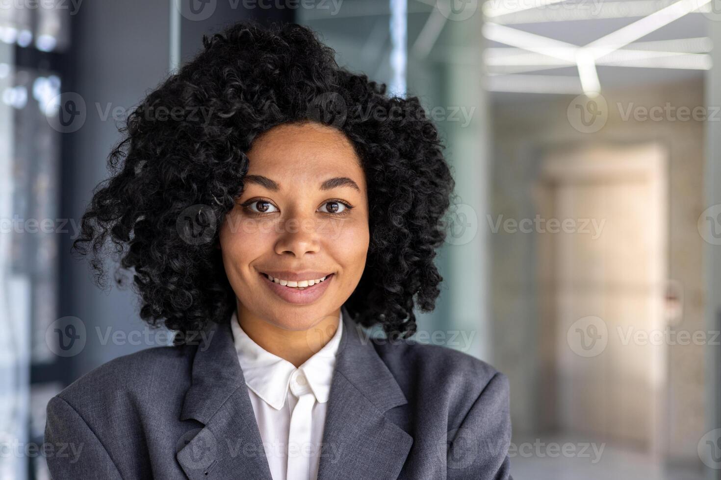 Beautiful african american woman close up inside office, businesswoman in business suit smiling and looking at camera, female worker at workplace inside office, boss satisfied and confident. photo