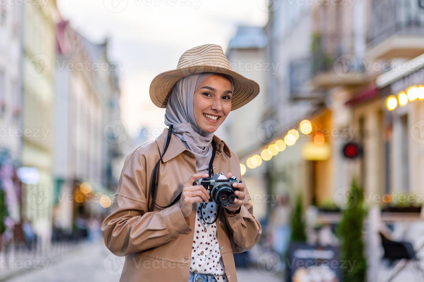 Portrait of young beautiful Muslim woman in hijab and hat, tourist walking in evening city with camera, woman traveling to different countries. photo