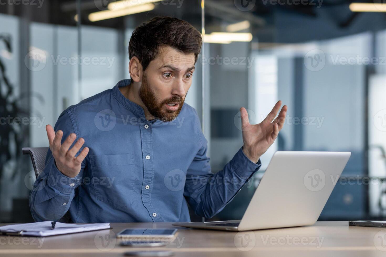 Shot of a startled male in an office setting, reacting with shock to something on his laptop screen. Captures the concept of unexpected news or error. photo