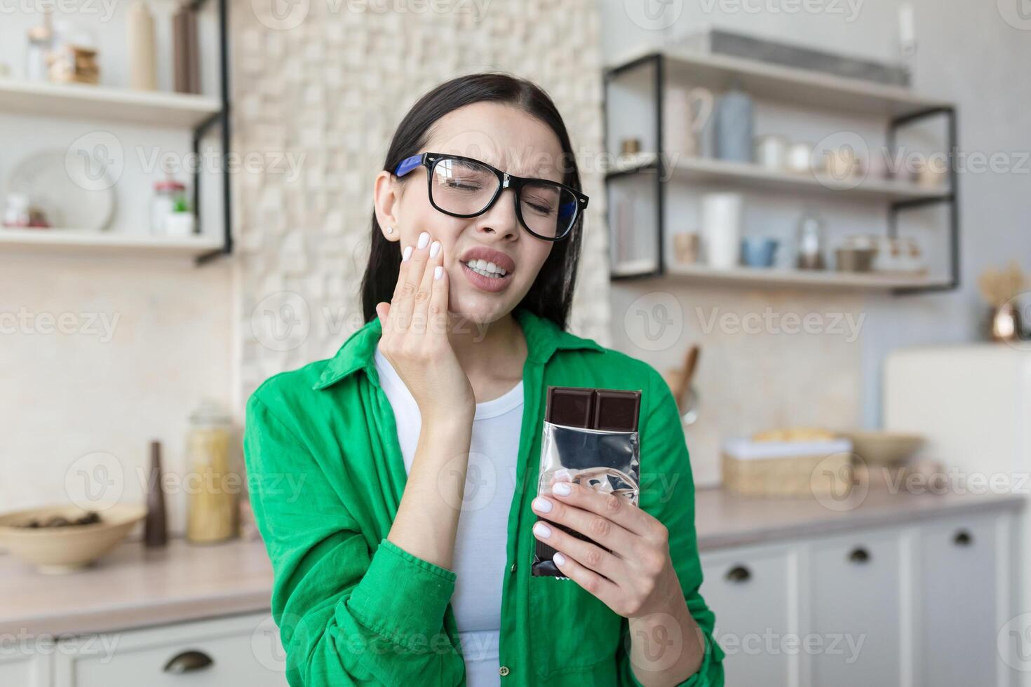 Young beautiful woman eating chocolate bar, having severe toothache at home. photo