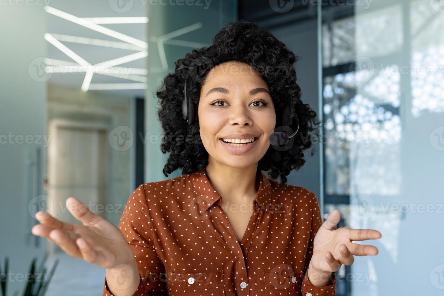Webcam pov view, call young beautiful woman with headset phone talking remotely with clients and partners, employee smiling and looking at camera, working inside office. photo