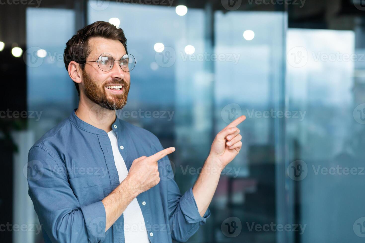 sonriente empresario dentro oficina señalando dedos a dirección, contento jefe en camisa y lentes. foto