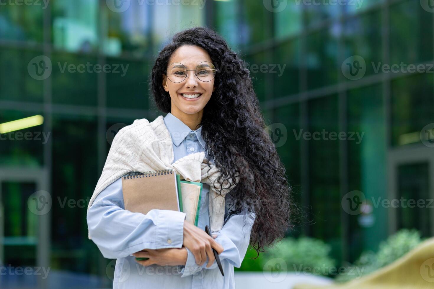 retrato de joven hermosa latín americano hembra alumno, mujer con libros y cuadernos sonriente y mirando a cámara, hembra profesor fuera de Universidad instalaciones oficina edificio. foto