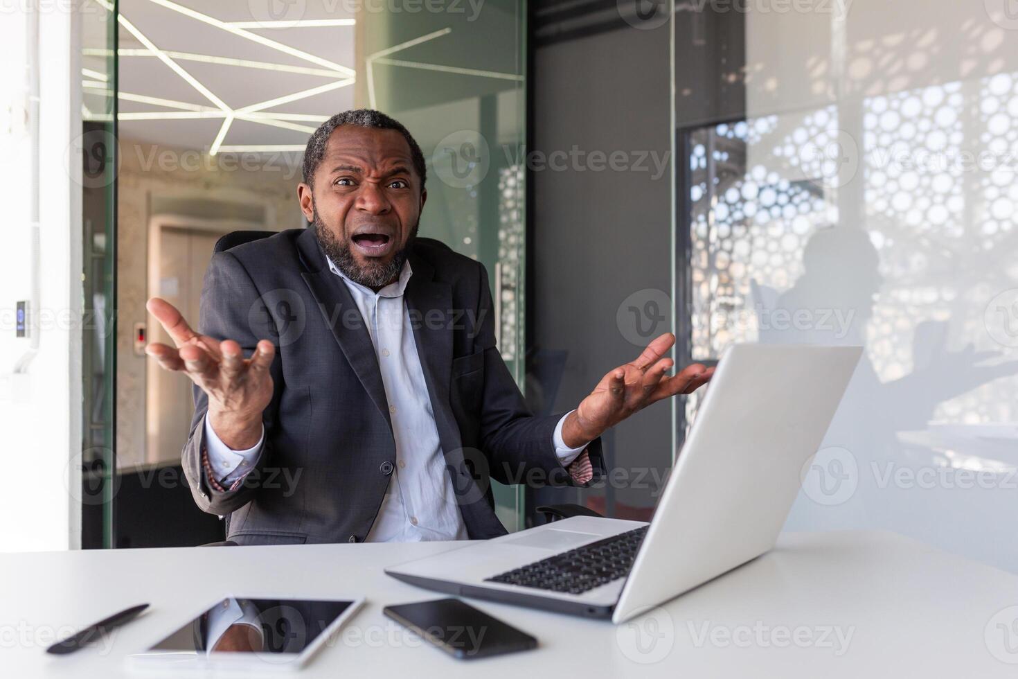 Frustrated angry boss looking at camera, senior gray haired mature man shouting upset, businessman inside office unhappy with achievement results, working with laptop. photo