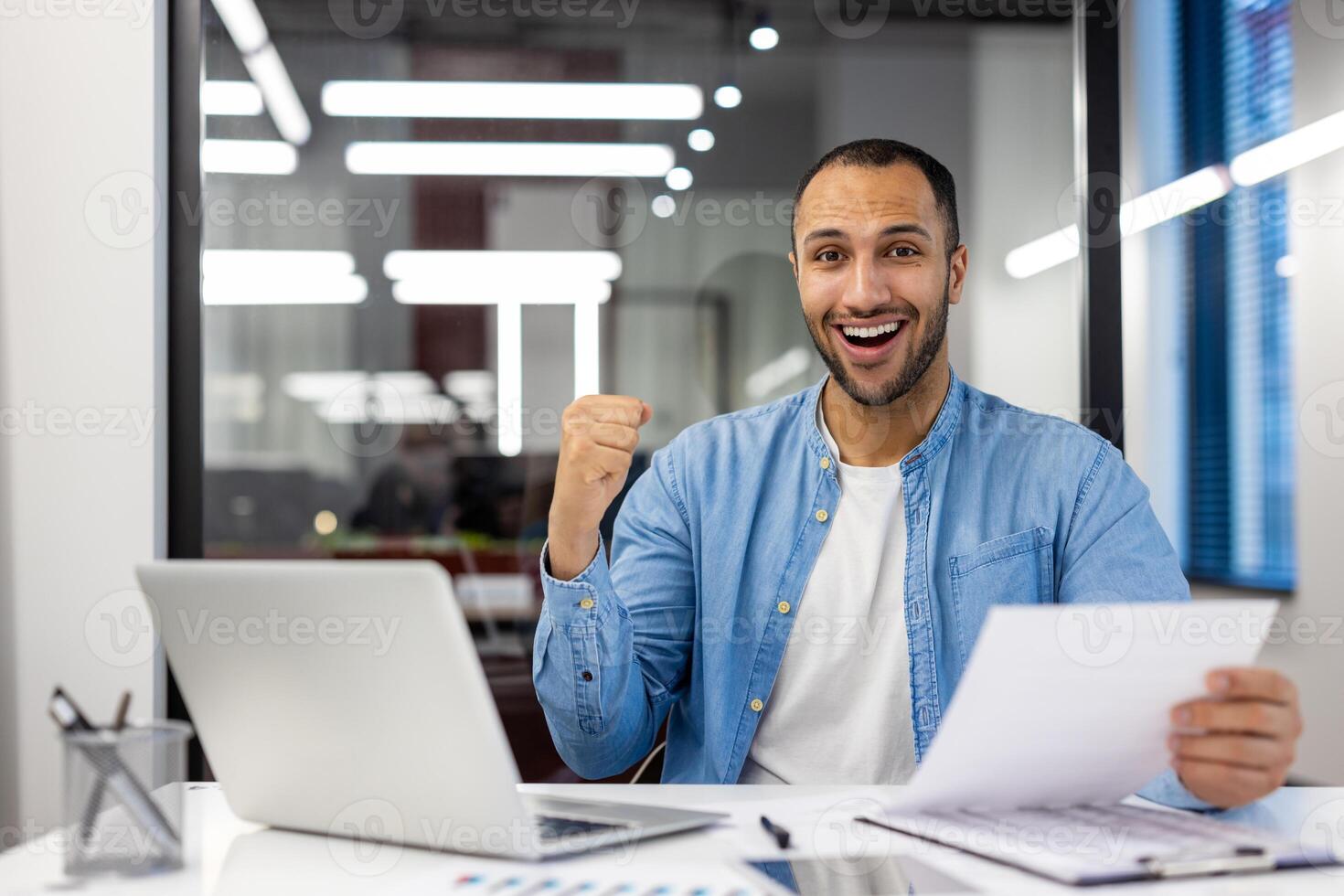 Successful Indian businessman fist-pumping in celebration at his modern office workspace, feeling excited and happy. photo