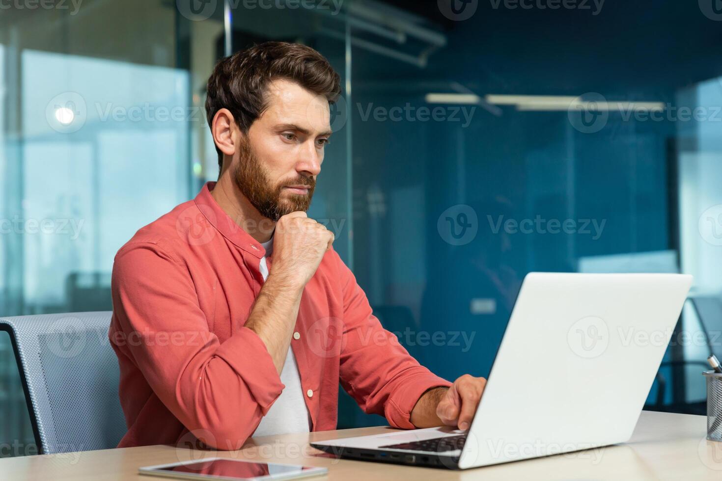 Serious thinking businessman close up, man in red casual shirt working inside modern office, mature boss working with laptop at workplace while sitting photo