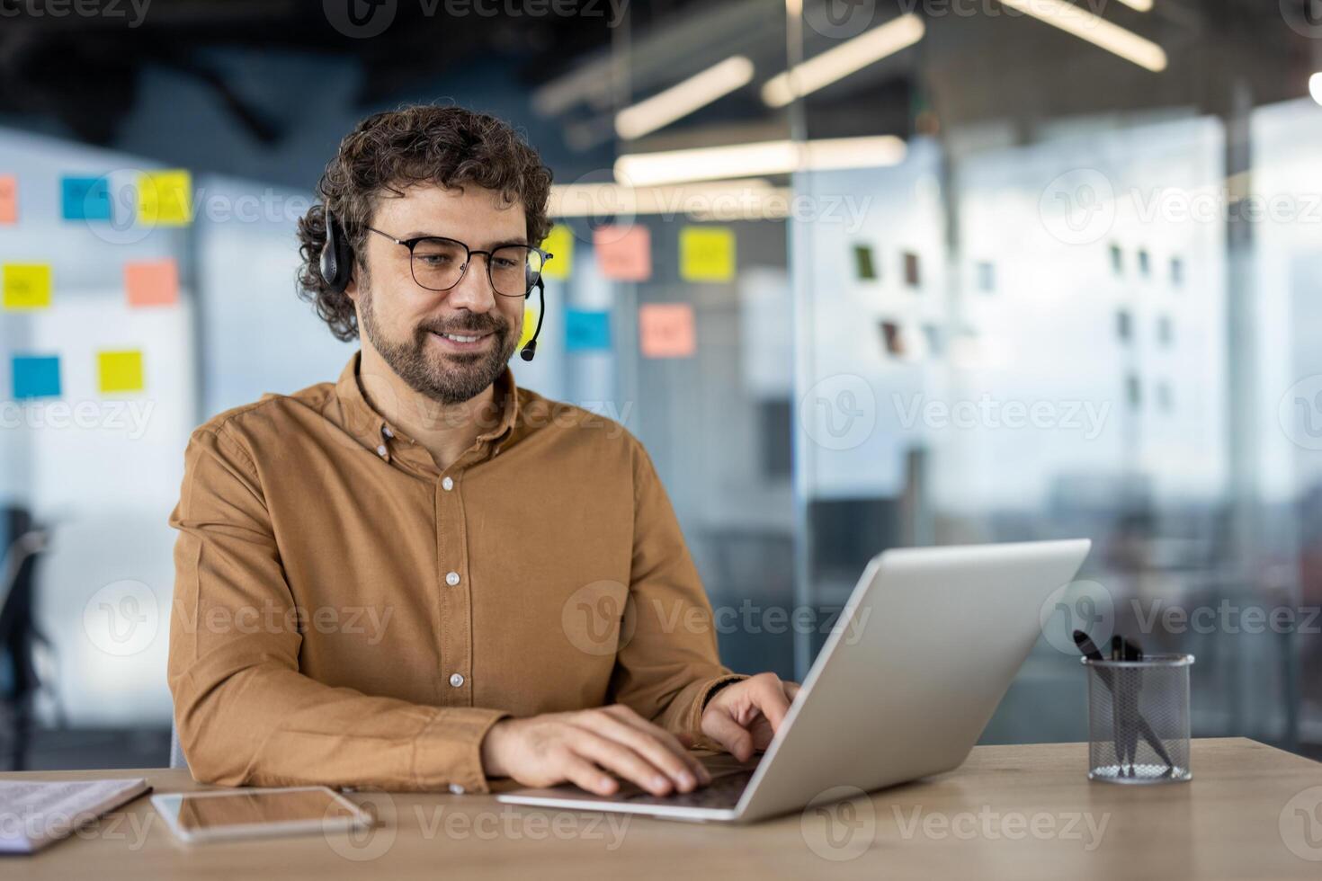 Cheerful male professional using laptop and wearing a headset in a modern office environment, displaying positivity and productivity. photo