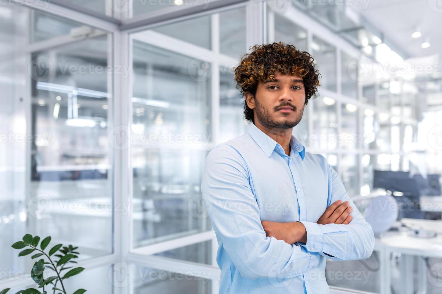 retrato de un exitoso joven Hispano programador en pie en un moderno oficina con su brazos cruzado en su cofre y mirando con confianza a el cámara. foto