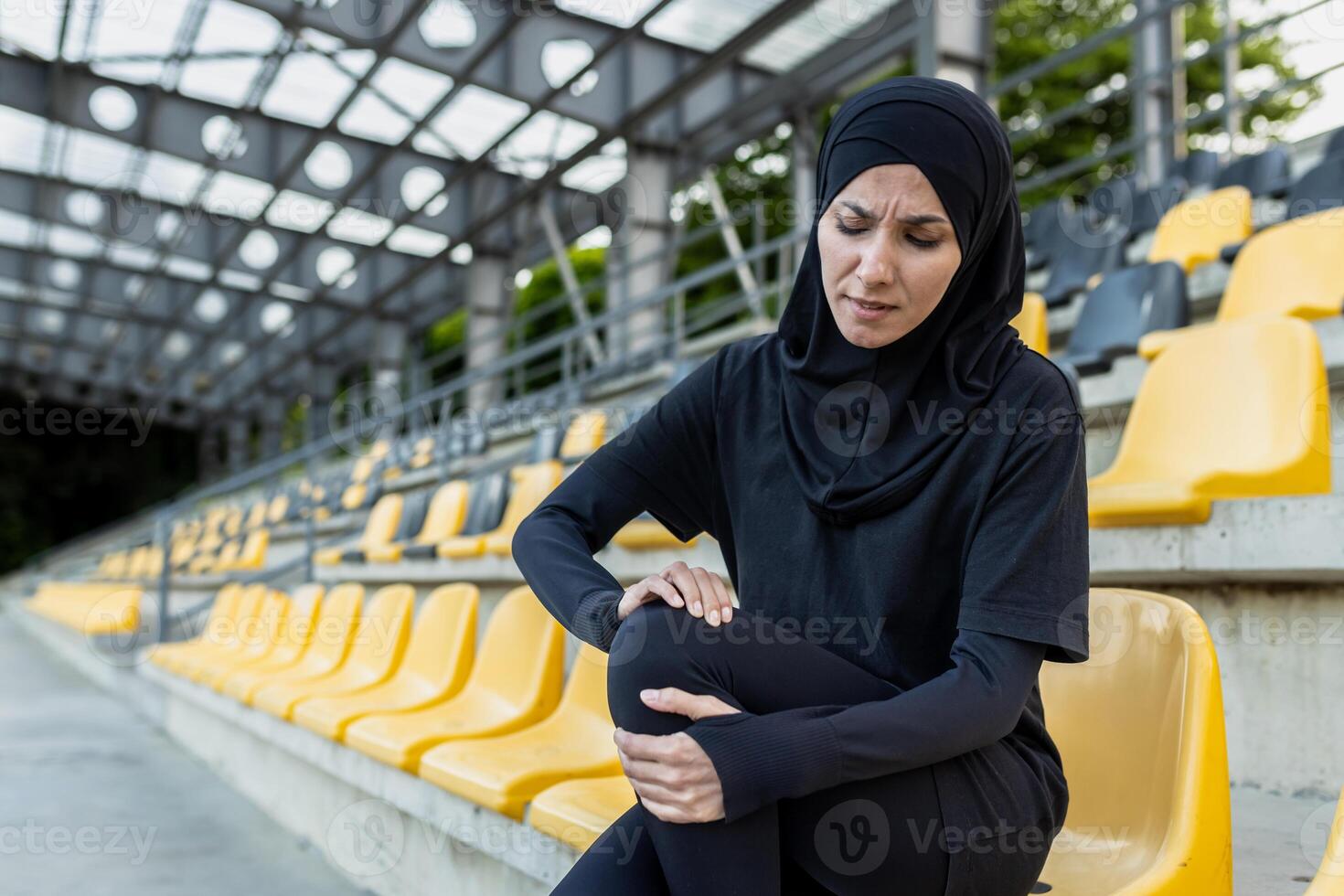 un mujer participación su rodilla en dolor mientras sentado en estadio pasos, sugerencia un relacionado con los deportes rodilla lesión. foto