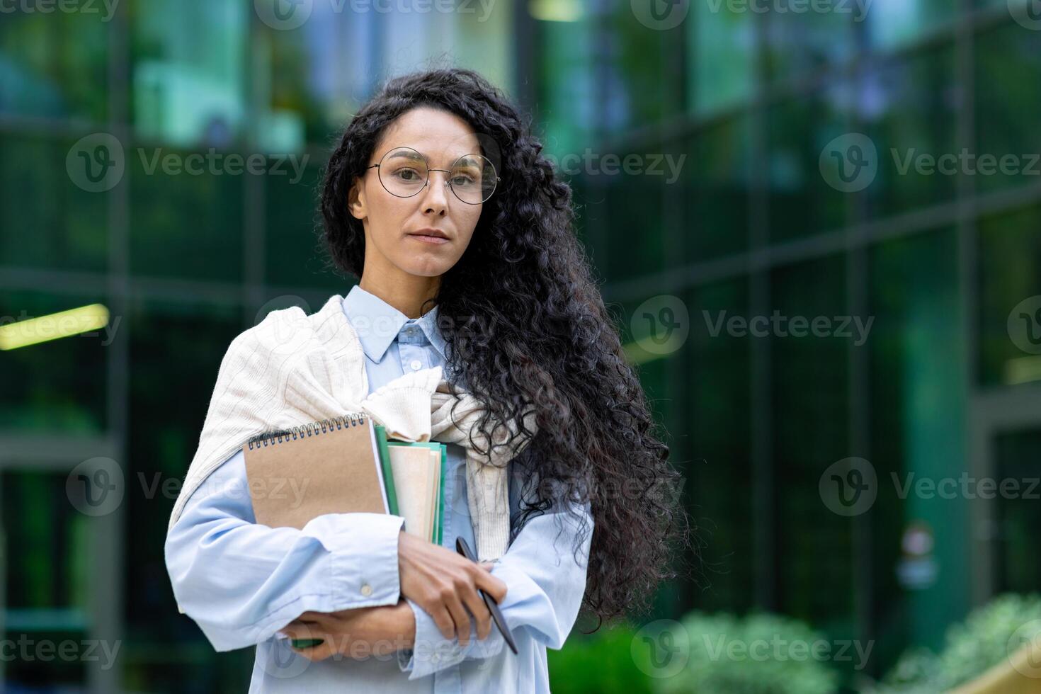 retrato de confidente indio hembra estudiante en pie en frente de oficina fuera de participación cuaderno mirando a cámara, joven oficina trabajador con Rizado oscuro pelo vistiendo lentes. foto