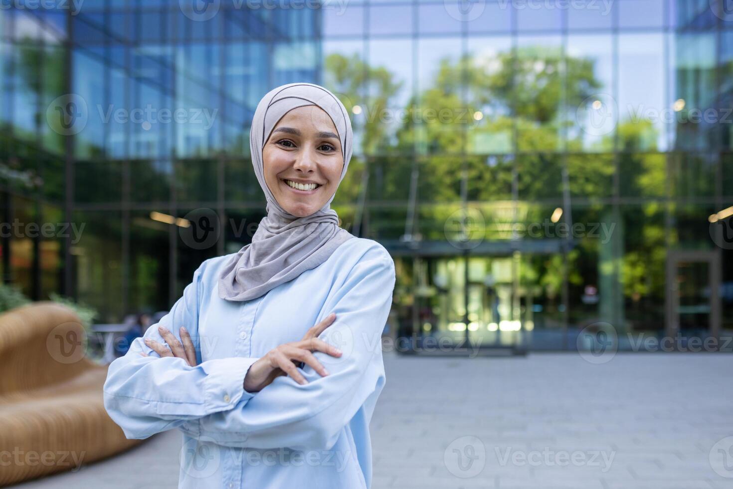 un profesional mujer en un hijab soportes con confianza con cruzado brazos fuera de un contemporáneo oficina edificio, simbolizando empoderamiento y diversidad en el lugar de trabajo. foto