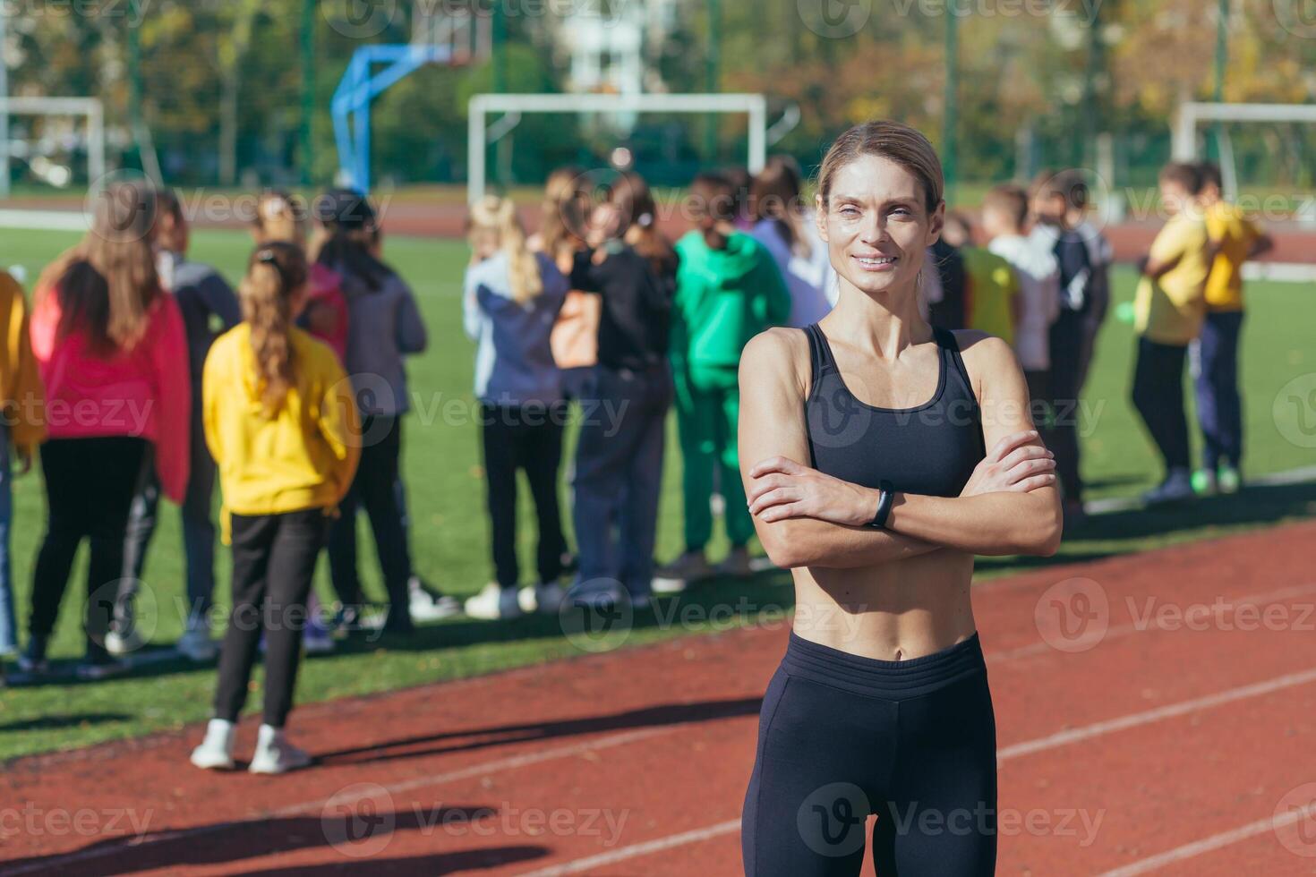 A female physical education teacher at school smiles and looks at the camera, an athlete trainer on the background of children, portrait. photo