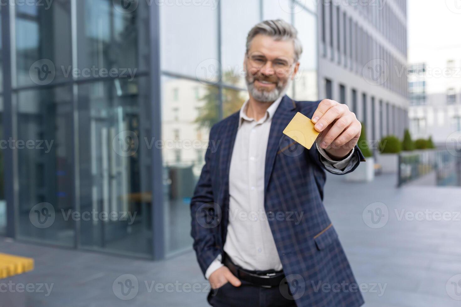 A smiling businessman in a suit holds a card in his hands, stands on the street in front of the office, looks at the camera. photo