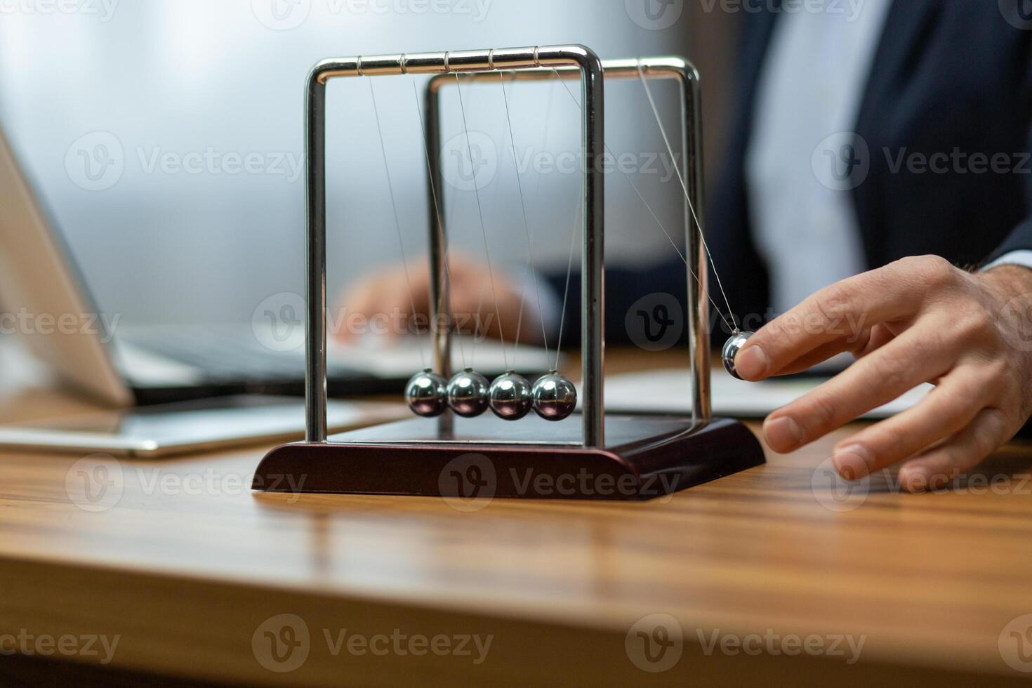 Mature businessman in a suit interacts with a Newton's cradle on his desk, symbolizing decision making and focus. photo