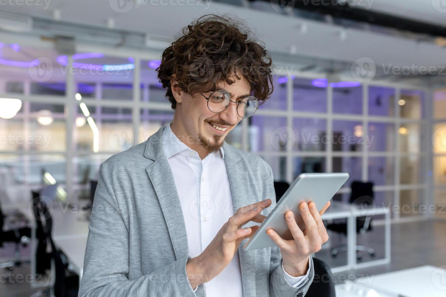 Content young male office worker using a digital tablet, the epitome of professional ease and technological proficiency in a bright office setting. photo