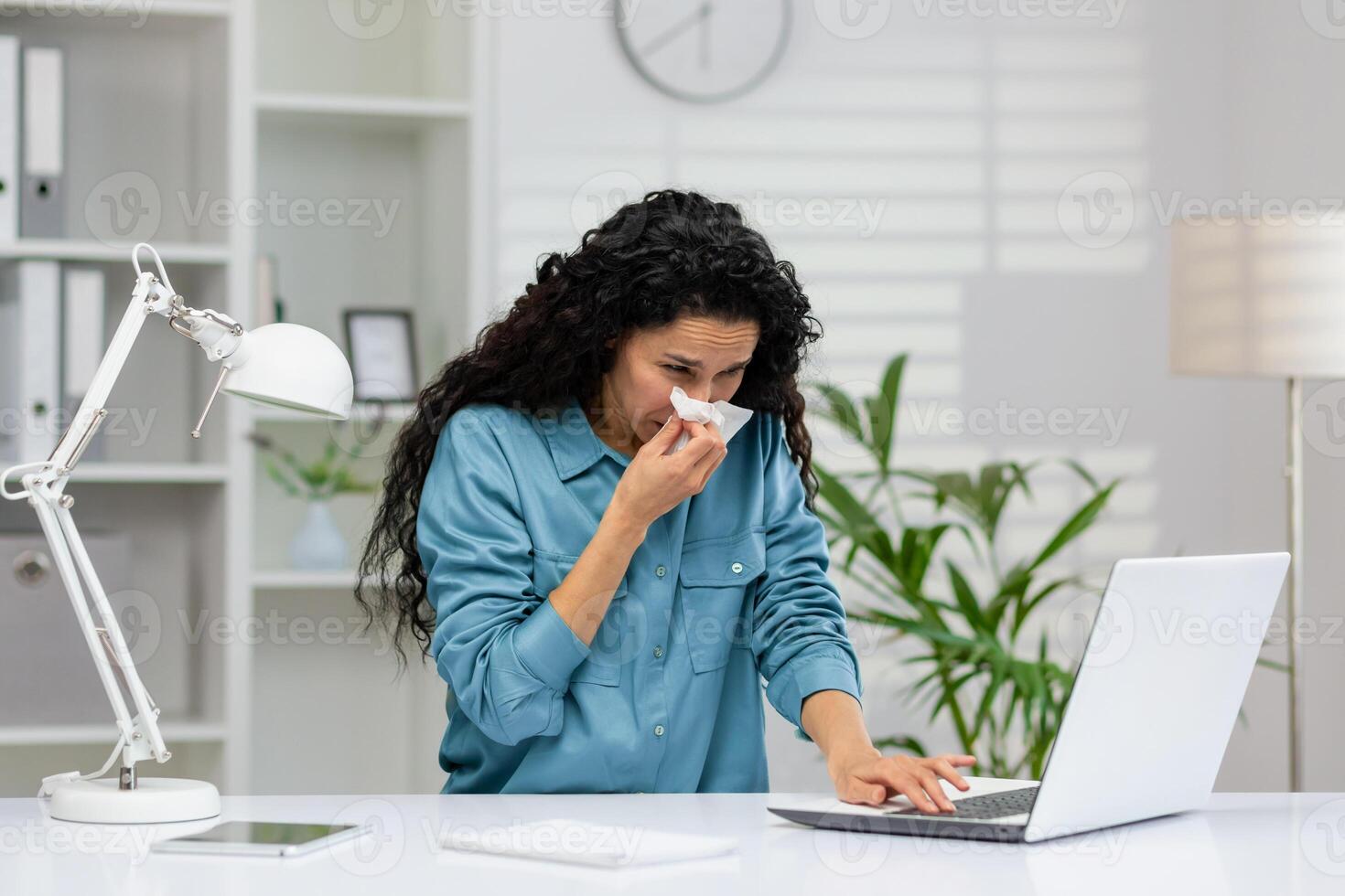 enfermo joven mujer de negocios utilizando un pañuelo de papel mientras trabajando a su oficina escritorio, demostración síntomas de un frío. foto