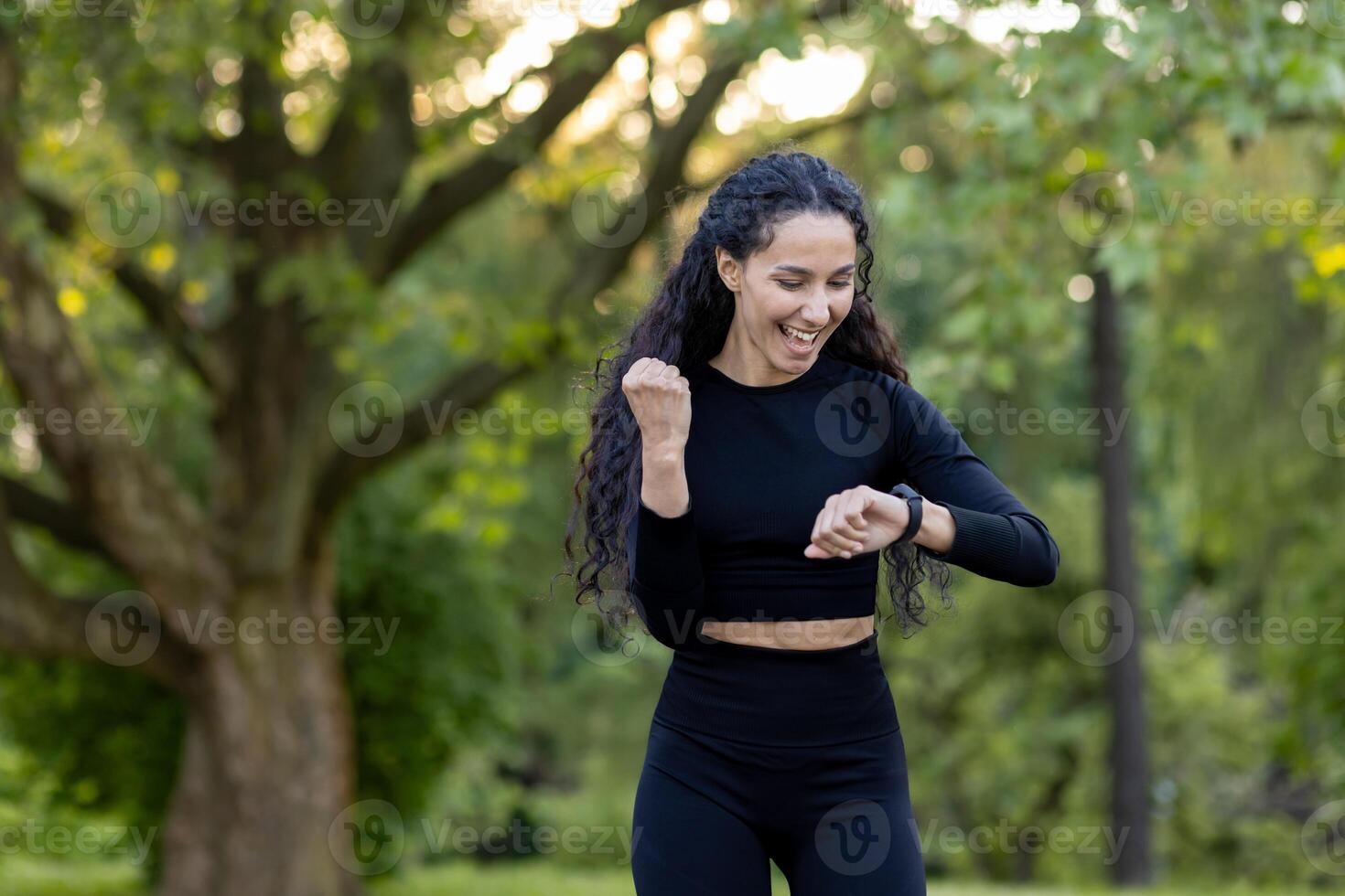 Joyful Hispanic woman checking her fitness tracker after a vigorous run in a serene park setting, expressing happiness and satisfaction with her progress. photo