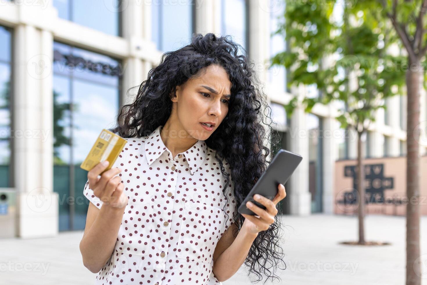 Upset and disappointed woman received money transfer error, Hispanic woman with bank credit card and phone cheated walking down street outside office building. photo