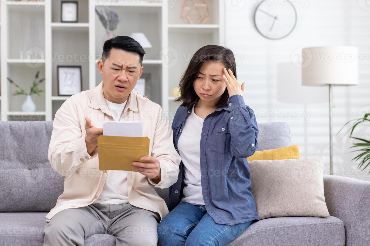 Upset Asian family, man and woman sitting together at home in living room on sofa, couple received letter mail envelope notification with bad news, unhappy with received message. photo