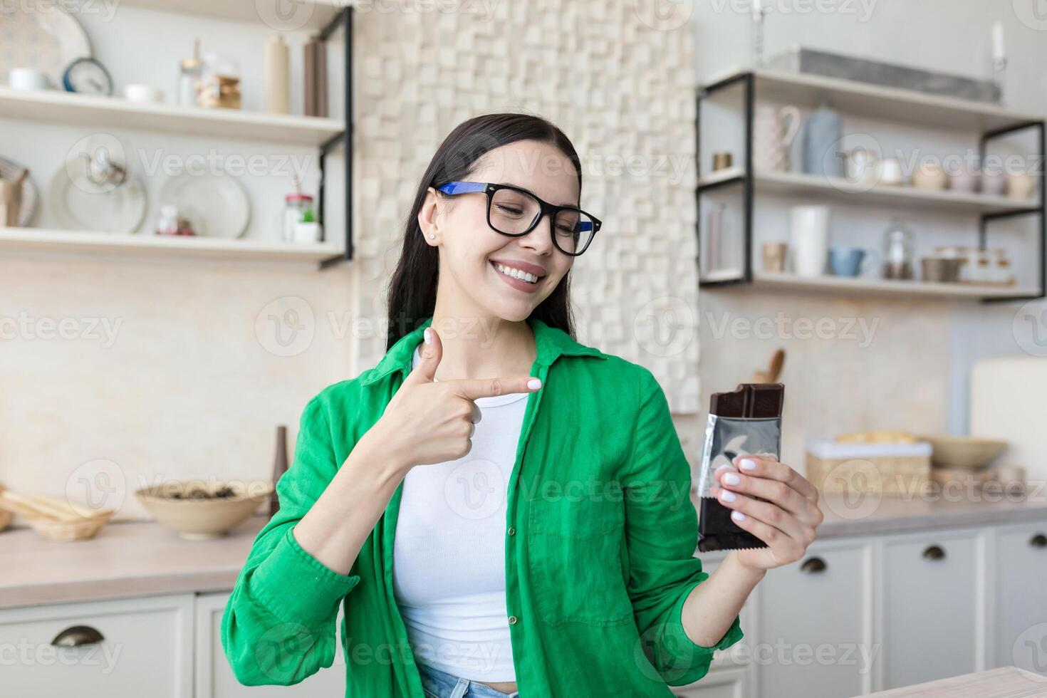 Young satisfied woman at home eating chocolate bar in kitchen photo