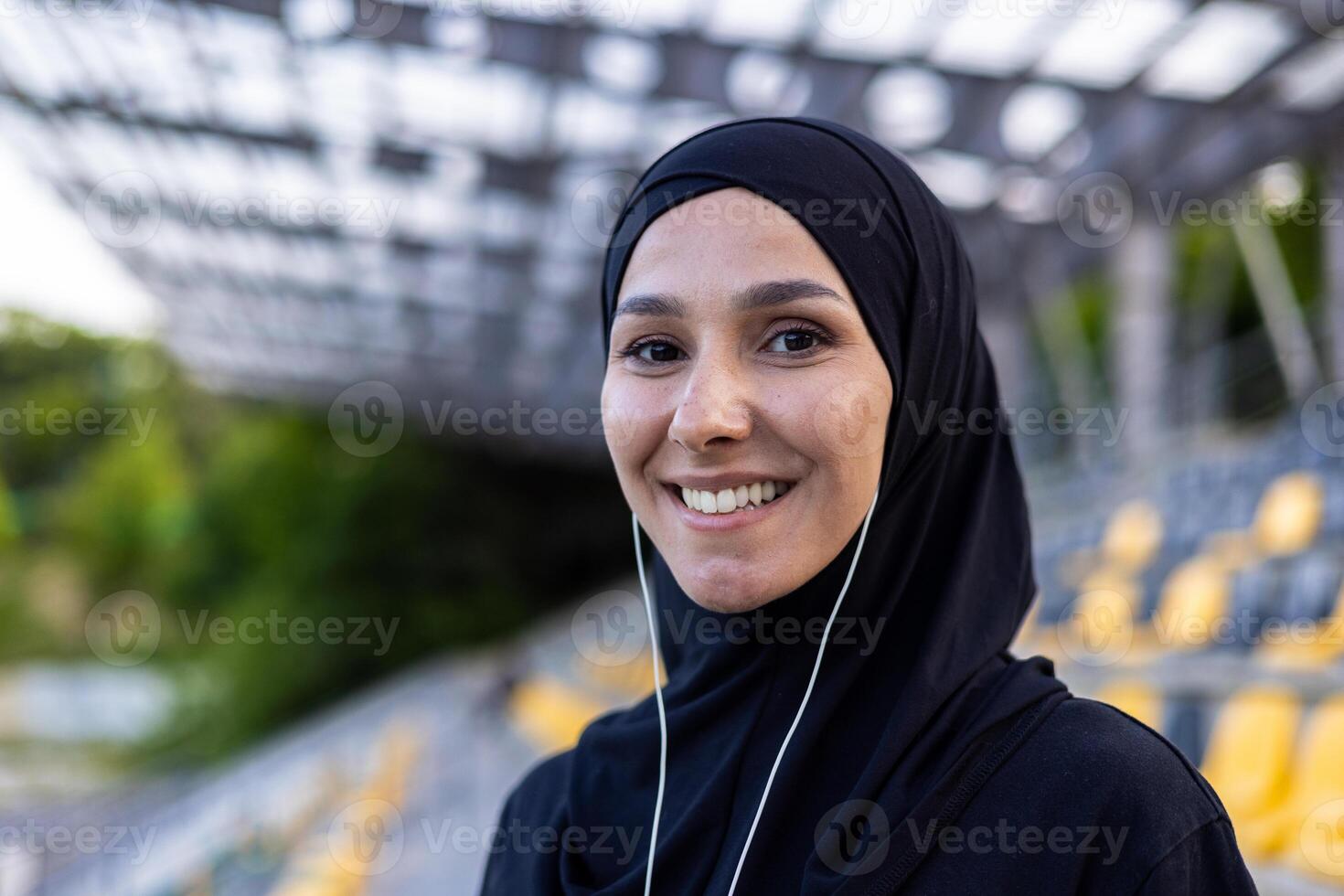 Portrait of happy muslim woman in hijab and headphones on court, doing sports and listening to music, smiling and looking at camera. photo