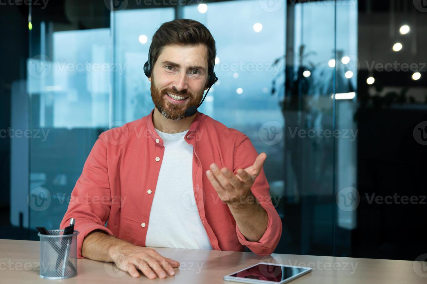 Webcam pov view, man in office with headset for call smiling and looking into camera, businessman seller online communicates with customers, works remotely laptop at online meeting colleagues photo