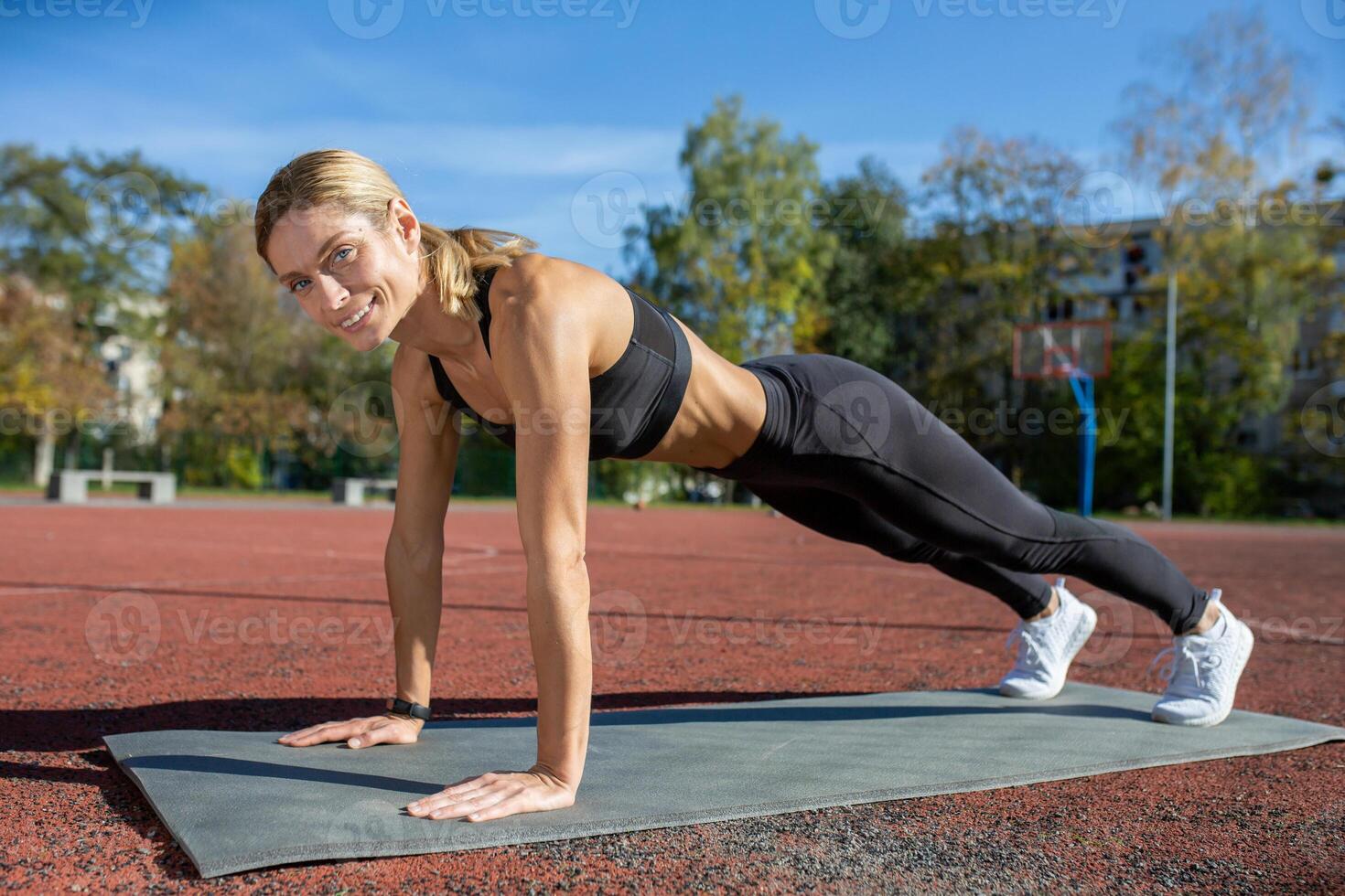 Fit woman in activewear doing a plank exercise on a mat at an outdoor court, showcasing strength and health. photo