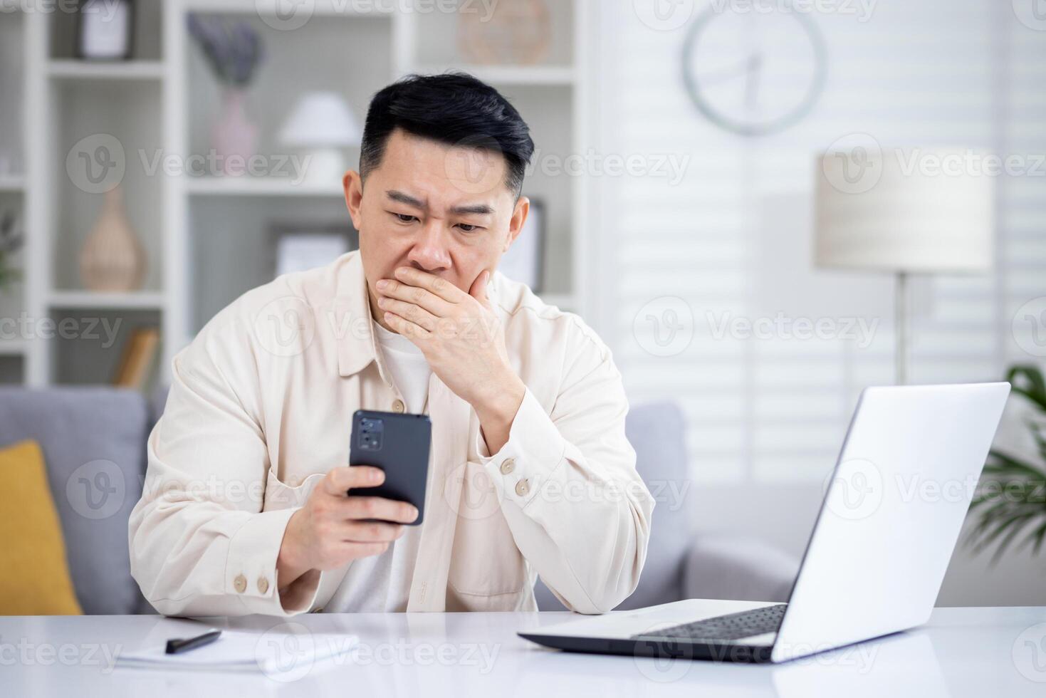 Asian mature man sitting alone at home on sofa in living room cinema, man received online notification message with bad news on phone, upset browsing internet pages using app on smartphone. photo
