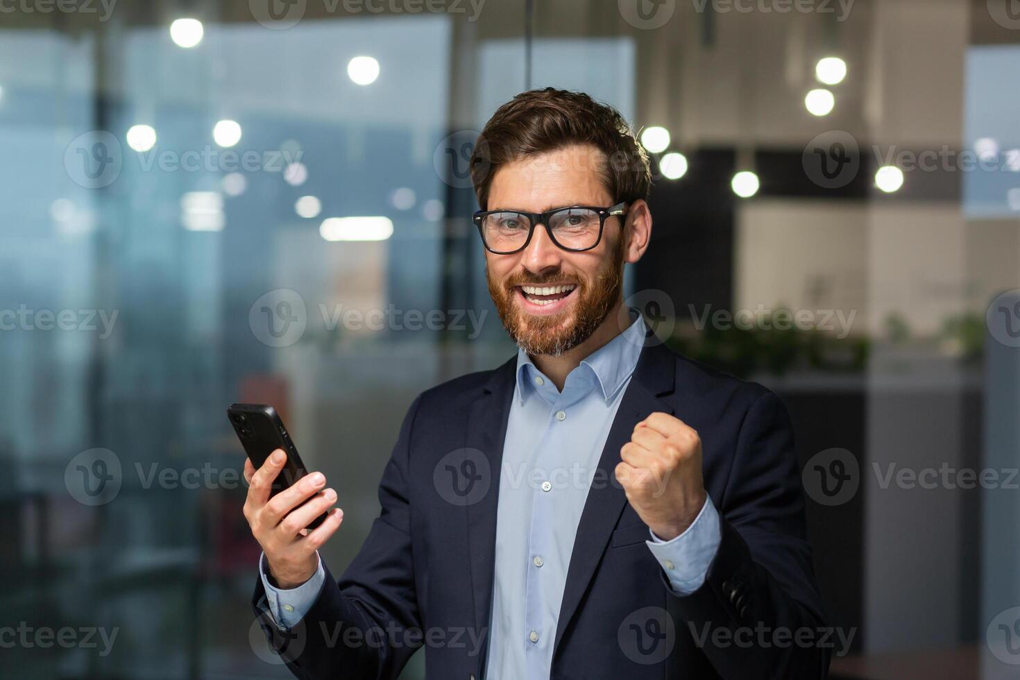 retrato de exitoso empresario inversor, maduro jefe en traje y lentes mirando a cámara y contento celebrando victoria éxito, hombre participación teléfono inteligente recibido en línea Noticias de bueno logro. foto