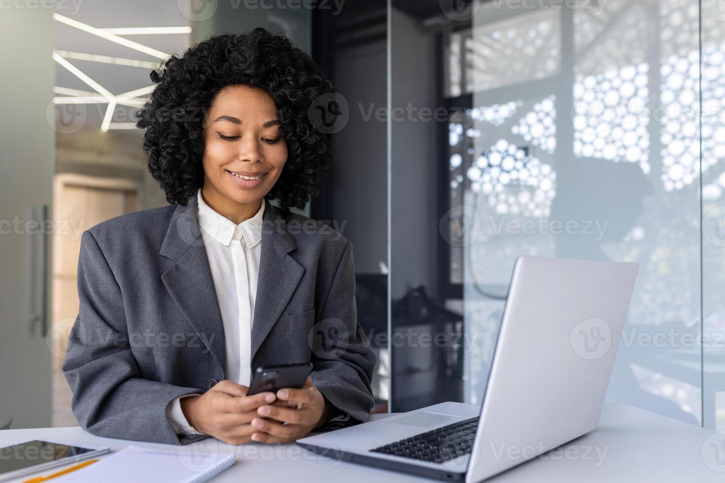Successful businesswoman at workplace inside office using phone, female worker reading message and smiling, african american woman holding smartphone using online application. photo