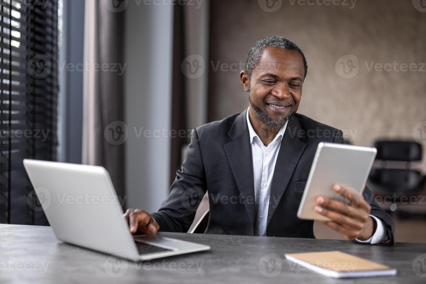 sonriente masculino en blanco camisa y negro chaqueta utilizando dos electrónico artilugio para mejoramiento de trabajando proceso. contemporáneo empresario conectando a crm sistema de empresa para en línea interactuando. foto