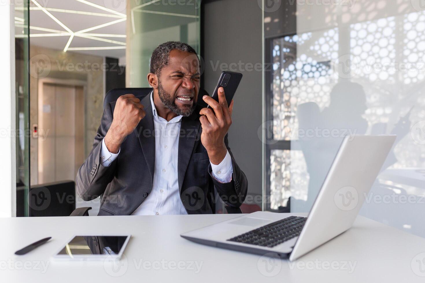 enojado irritado jefe gritos en el teléfono, empresario insatisfecho con el conversacion se sienta dentro el oficina, hombre a el lugar de trabajo en un negocio traje trabajos con un ordenador portátil. foto