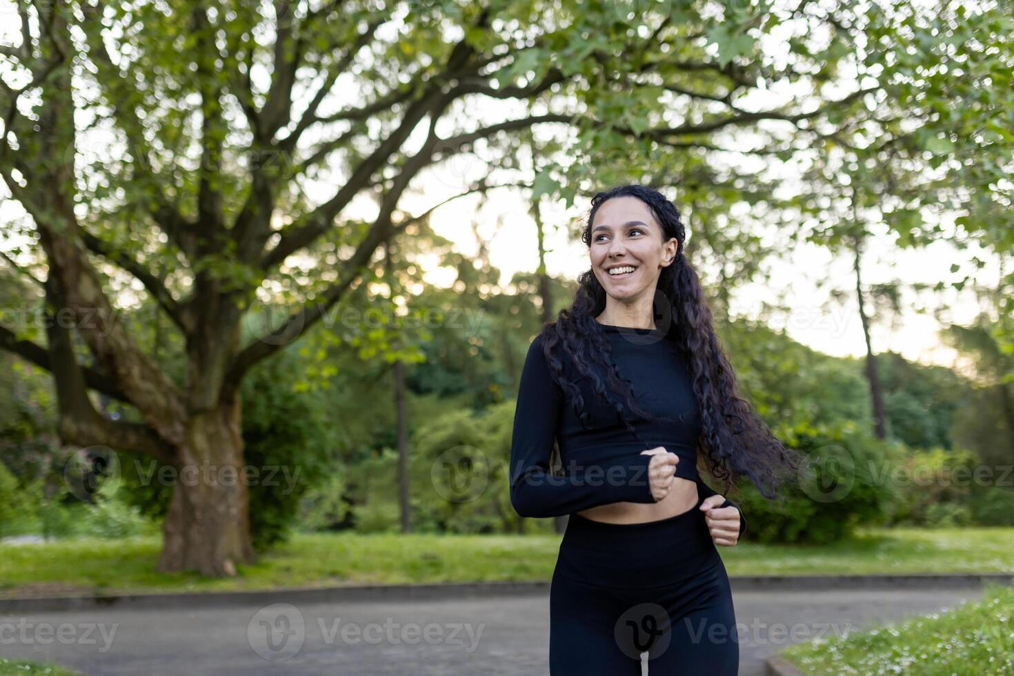 Smiling female runner in sportswear jogging in a green park at dusk, portraying the joy of outdoor exercise and well-being. photo